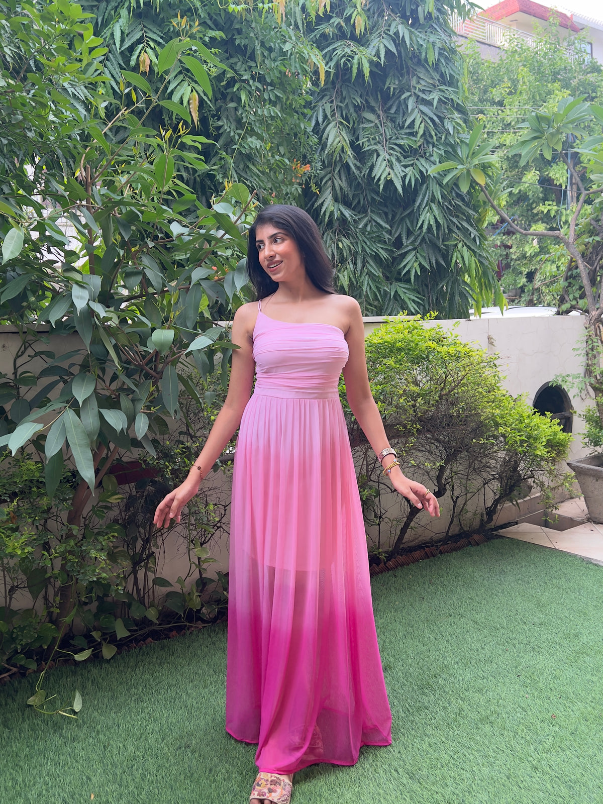 Pink ombre one-shoulder maxi dress with pleated sheer skirt and corset back, worn outdoors